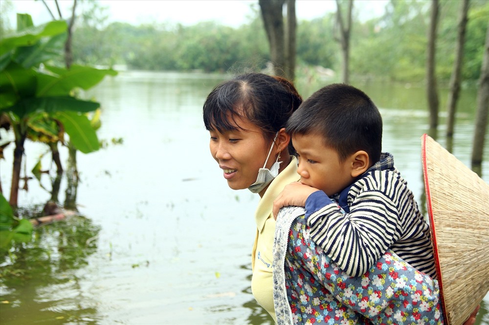 Người mẹ cõng con nhỏ, vượt qua dòng nước ngập.