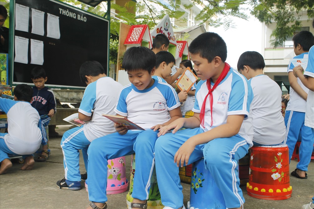 Các em học sinh thích thú ngồi đọc sách trên những thùng sơn đầy màu sắc. Ảnh: T.H