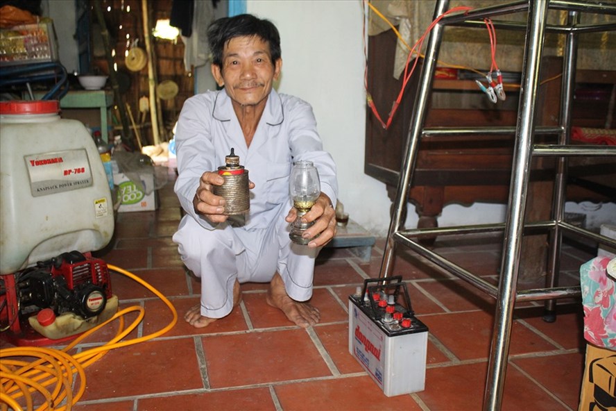 Ông Sang bên chiếc bình ắc quy vừa sắm để cải tiến thay vì đã dùng đèn dầu 30 năm nay. Ảnh: TRẦN TUẤN