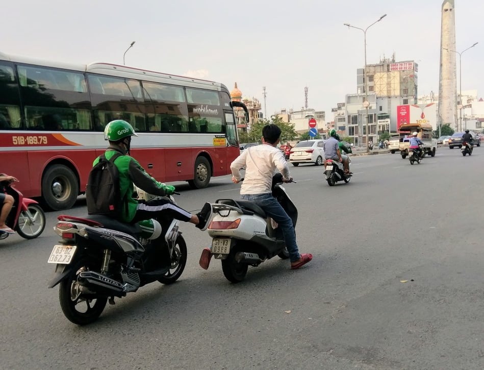 Một tài xế xe ôm công nghệ vừa chạy xe vừa dùng chân đẩy xe máy khác. Ảnh: M.Q