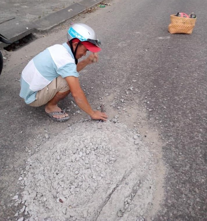 Anh Hùng ngồi đục mảng bê tông rơi vãi trên mặt đường để người khác khỏi nguy hiểm.