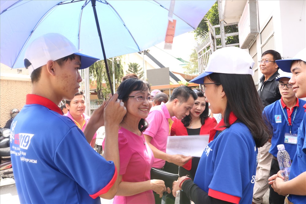 Không chỉ quan tâm cho thí sinh, các tình nguyện viên còn đến trò chuyện, che nắng cho các phụ huynh đợi con ở điểm thi. Ảnh: Anh Tú