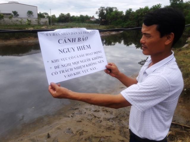 Phó Trưởng Công an xã Thạch Đài Bùi Văn Tuyến bên tờ thông tin cảnh báo về cá sấu. Ảnh: Trần Tuấn