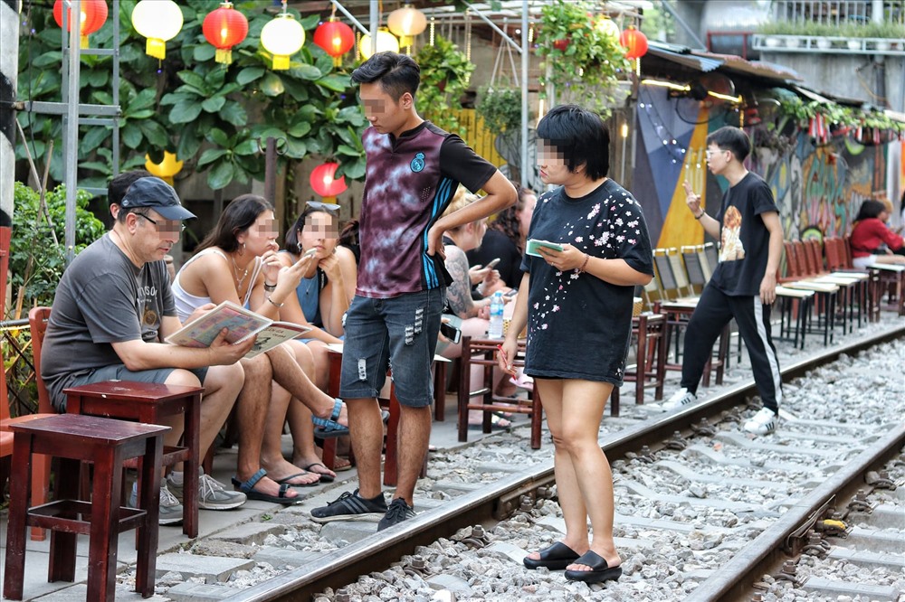 Nhiều du khách vô tư ngồi sát đường tàu vui chơi, uống cà phê. Ảnh: Thái Hà.