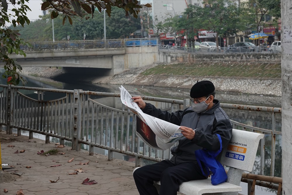 Ông Phạm Phi Hồng, nhà sát sông Tô đoạn chảy qua phường Kim Giang, phải đeo khẩu trang khi ngồi đọc báo.