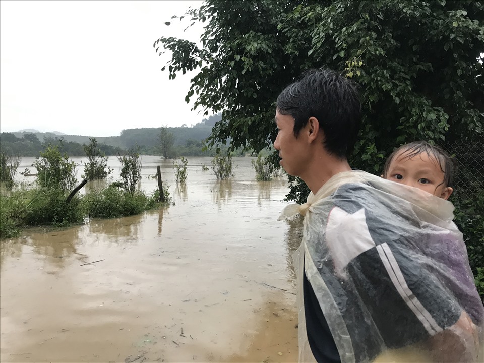 Một người dân đứng cõng con lặng nhìn dòng nước lũ. Anh này cho hay, đang chờ chính quyền bồi thường, bố trí tái định cư mới. Hơn 10 năm qua, gia đình tôi vẫn cứ mãi kẹt trong vùng dự án. Ảnh: B.T
