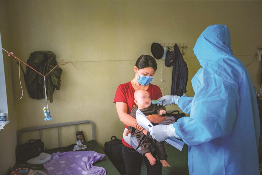 Cán bộ quân y đo thân nhiệt cho một cháu bé đang thực hiện cách ly cùng mẹ tại Trường Quân sự tỉnh Hoà Bình sau khi trở về từ vùng dịch Hàn Quốc. Ảnh: Lưu An Nhiên