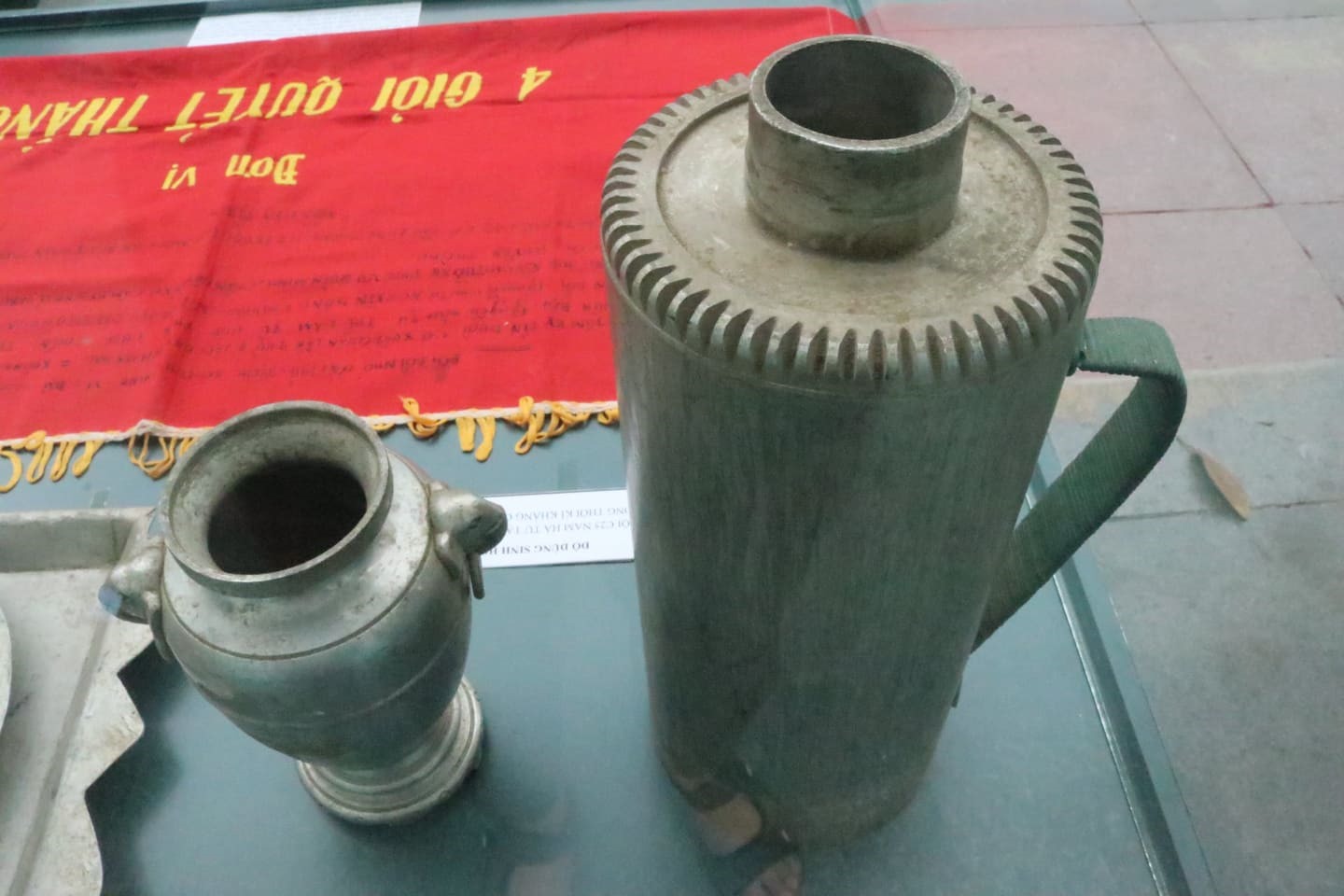 Cờ “Đơn vị 4 giỏi quyết thắng” và những vật dụng sinh hoạt được chế tạo từ xác máy bay trưng bày trong khuôn khổ triển lãm. Ảnh: Lan Nhi