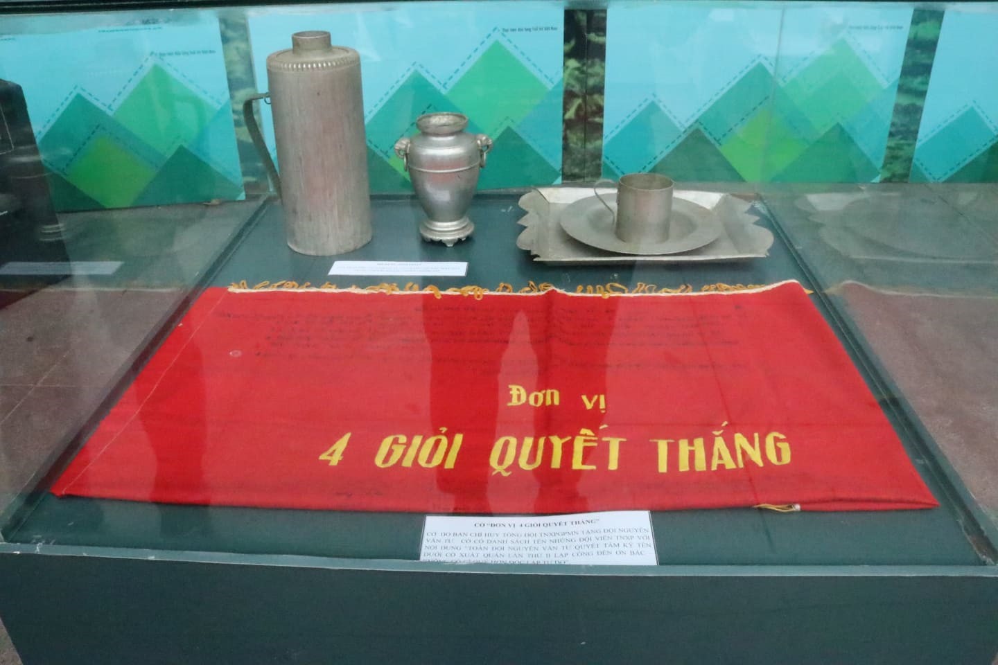Cờ “Đơn vị 4 giỏi quyết thắng” và những vật dụng sinh hoạt được chế tạo từ xác máy bay trưng bày trong khuôn khổ triển lãm. Ảnh: Lan Nhi
