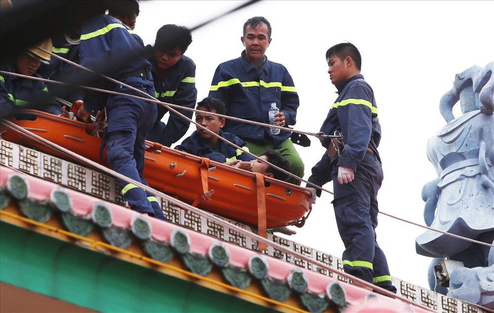 Để anh ta khỏi giãy giụa cũng như đưa xuống đất an toàn, cảnh sát cố định thanh niên này vào máng trượt chuyên dụng rồi đưa xuống khỏi nóc ngôi chùa bằng dây thừng. Ảnh: Trường Sơn