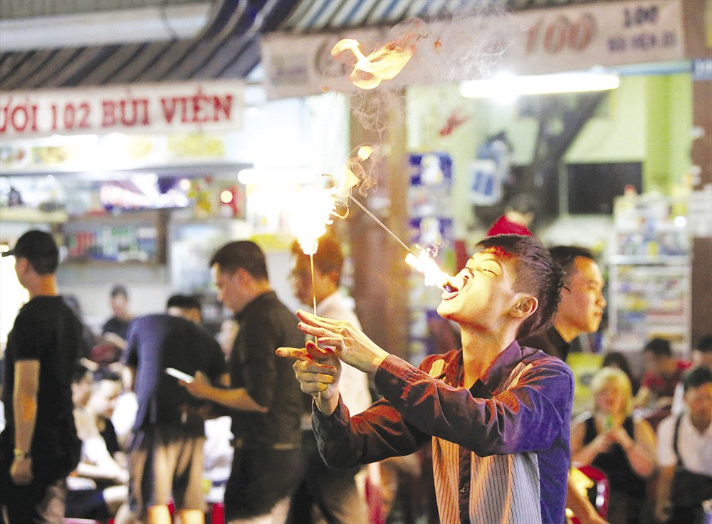 Trong ảnh là một thanh niên đang mưu sinh bằng nghề nuốt lửa, dao lam trên đường Bùi Viện. Công việc của anh là trình diễn màn nuốt lửa và nhai nát một con dao lam. Để thu hút sự chú ý của khách, trước khi trình diễn, anh thường hô lớn một hoặc vài tiếng, khi nào thấy nhiều người chú ý vào mình thì anh mới trình diễn.