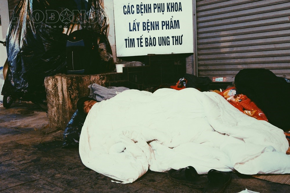 Gió lạnh kết hợp với mưa phùn khiến người vô gia cư ngủ vỉa hè phải quấn chăn, áo mưa kín mít quanh người.