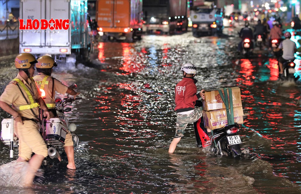 Trong dòng nước đen xì, một thanh niên chở hàng bị té ngã. Ngay lập tức, tốp CSGT của Trạm cSGT Tân Túc - PC67-Công an TPHCM liền tiếp cận để giúp đỡ. Ảnh: Trường Sơn