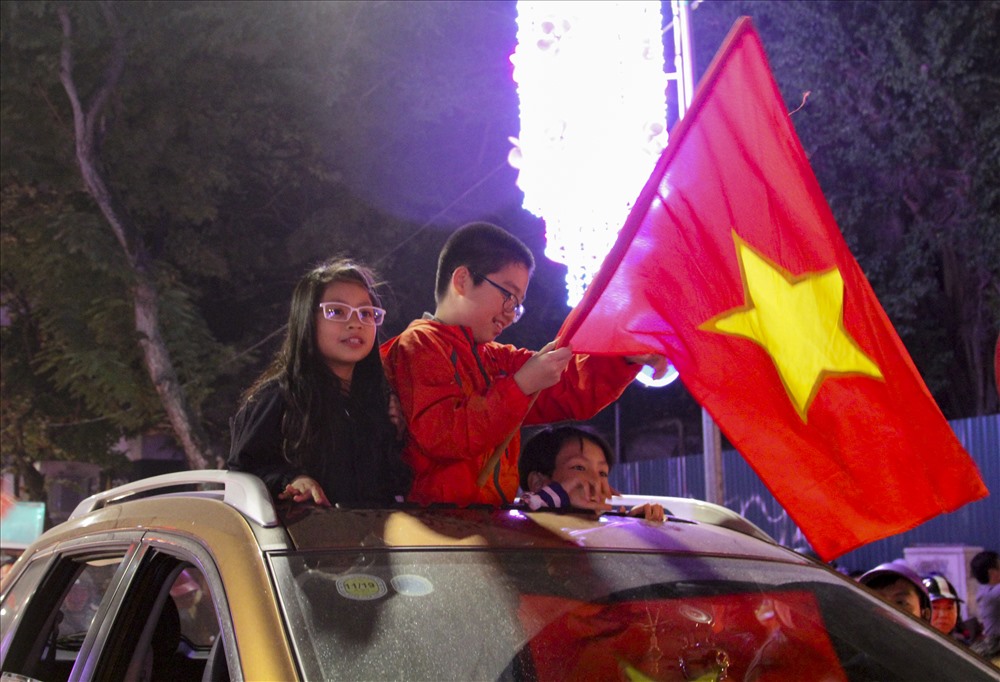 Các em nhỏ chui lên cửa sổ trời của xe hơi để vẫy cờ và reo hò cùng đoàn người