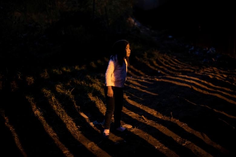 Một bé gái Honduras nhìn qua hàng rào, bước qua hàng rào này là miền đất hứa hẹn. Nhiều di dân đang cảm thấy thất vọng vì bị kẹt lại quá lâu ở thành phố Tijuana, nơi họ phải sống trong điều kiện thiếu thốn. Ảnh: Reuters.