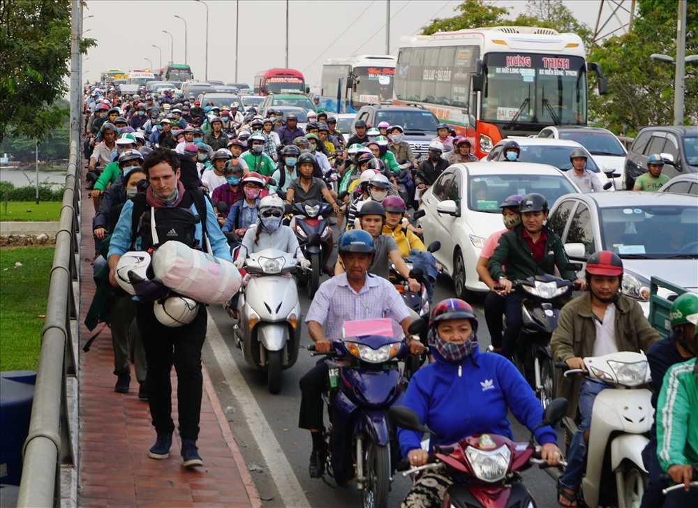 Một người nước ngoài đeo lỉnh kỉnh đồ đạc trên đường cuốc bộ trên cầu Bình Triệu