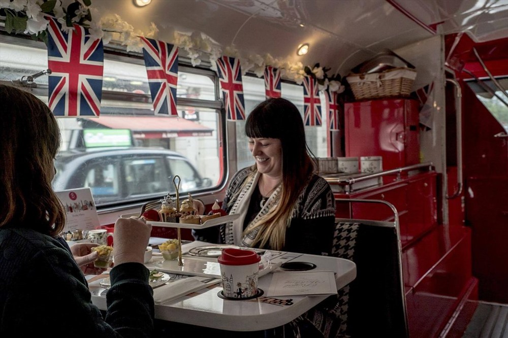 Hành khách trong chuyến thăm quan bằng xe buýt ở London, trên xe được trang trí cờ hoa rực rỡ. Ảnh: NYT.