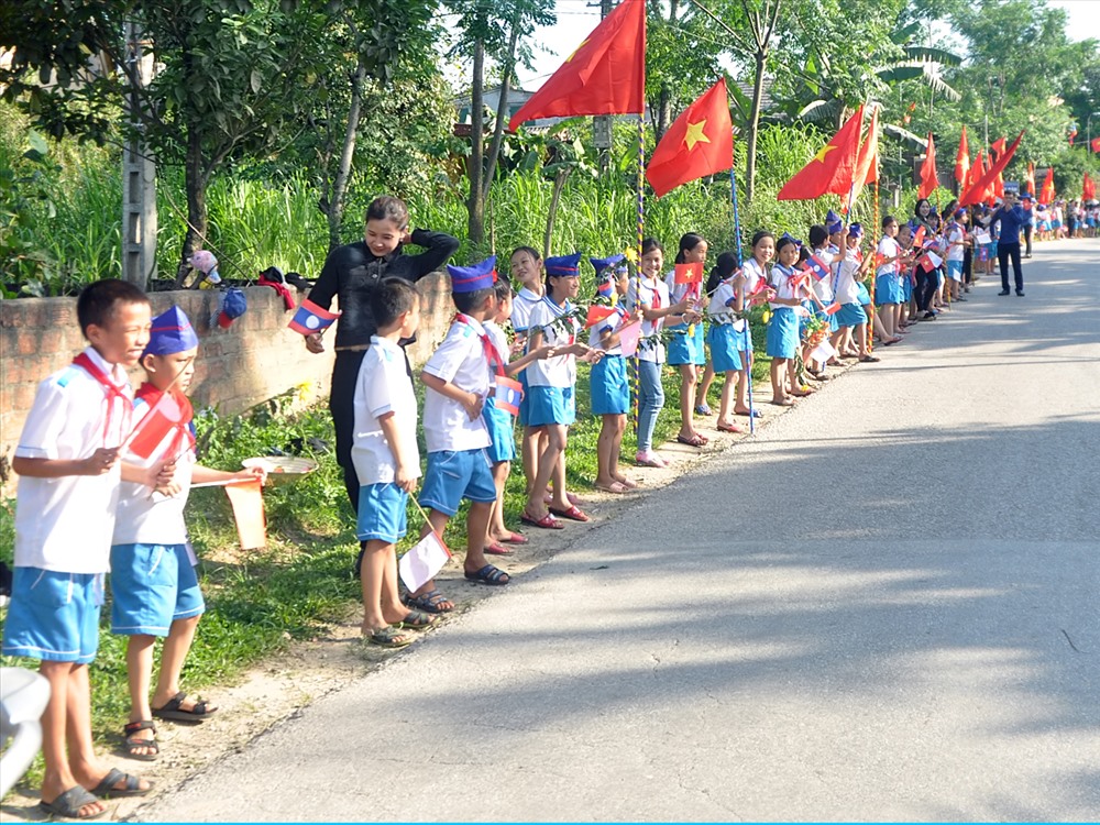 Người dân và các cháu học sinh đứng chật 2 bên tuyến đường quốc lộ 8A, trên tay cầm lá cờ hai nước Việt-Lào để chào đón các anh hùng liệt sĩ trở về. Ảnh: Minh Lý