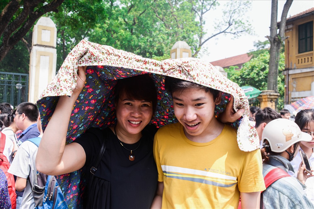 Tiếng trống báo hiệu giờ thi kết thúc, khi các thí sinh rời địa điểm thi, phụ huynh cởi áo làm bóng mát cho con.