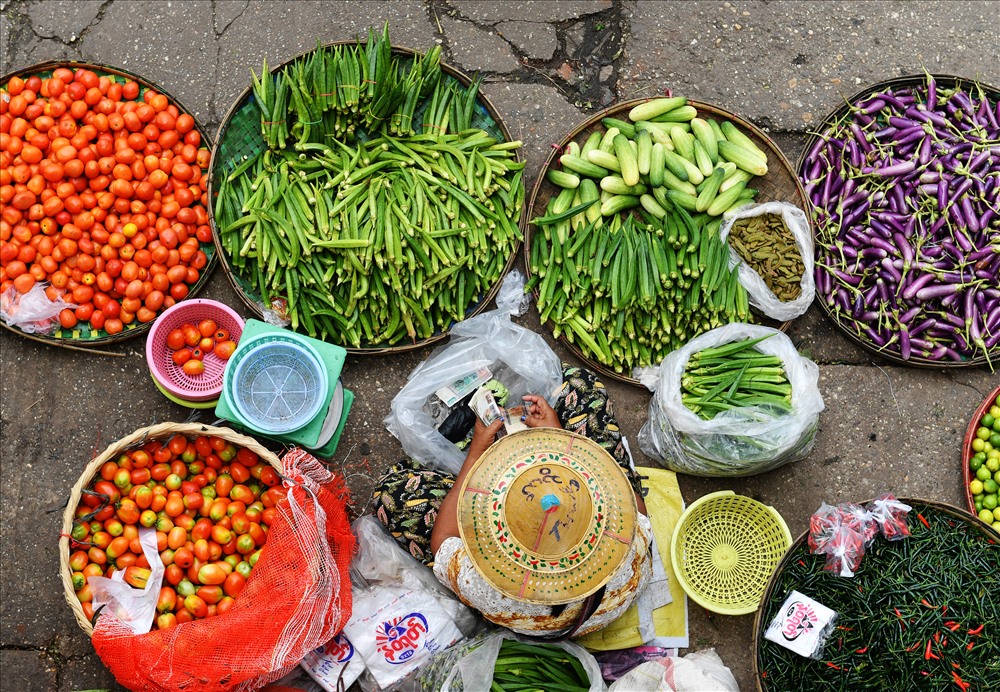 Người phụ nữ Miến với chiếc mũ truyền thống, ngồi bán hàng dưới nắng.