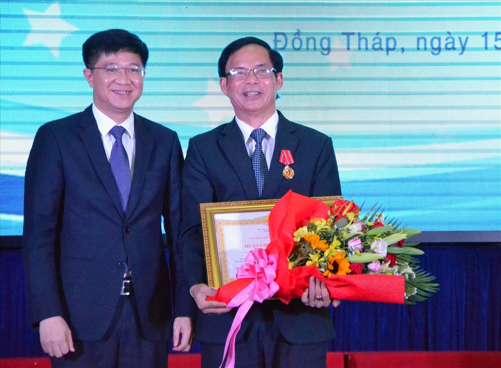 Thay mặt Bộ GDĐT, TS. Trịnh Xuân Hiếu, Vụ trưởng Vụ Thi đua Khen thưởng (trái) trao Huân chương Lao động hạng Nhì và hoa chúc mừng PGS.TS Nguyễn Văn Đệ. Ảnh: Lục Tùng