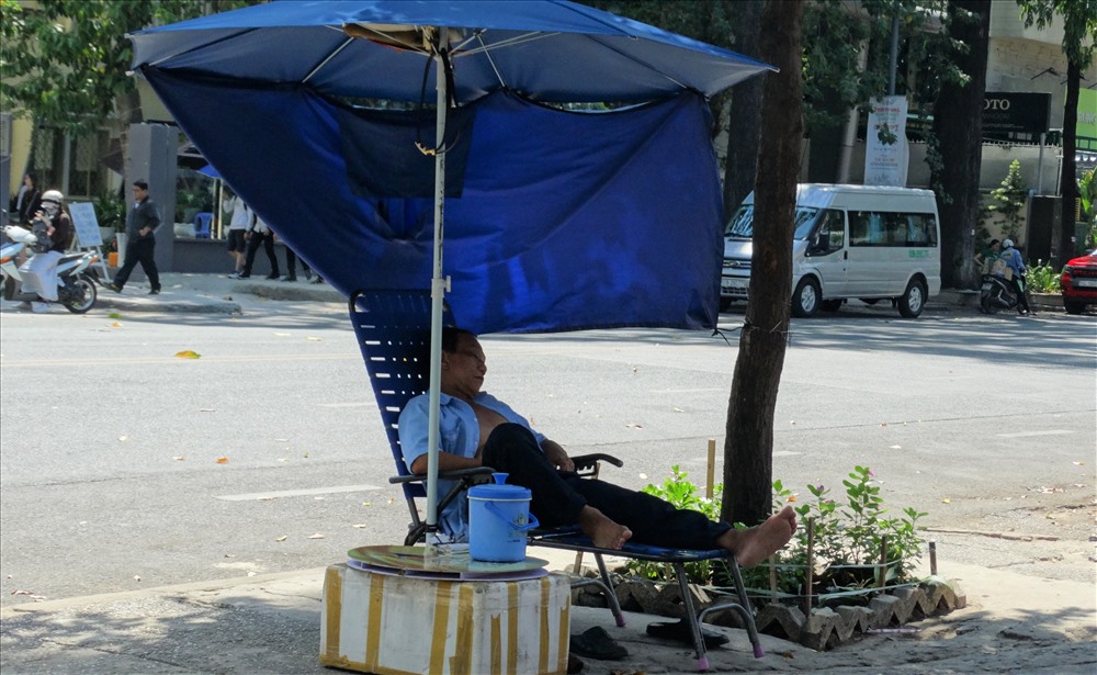 Một bác bảo vệ tận dụng chiếc dù và áo mưa để làm công cụ tránh nóng cho giấc ngủ trưa.