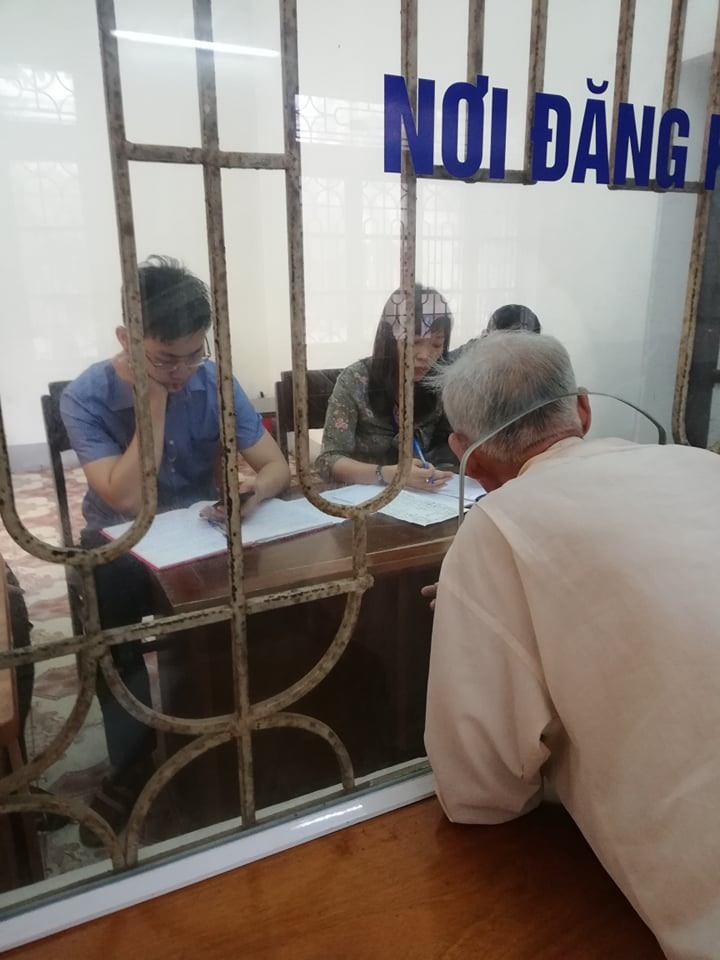Người dân phải chui qua lỗ kính nhỏ để làm việc với cán bộ, trong khi đó cán bộ thì đang sử dụng điện thoại.